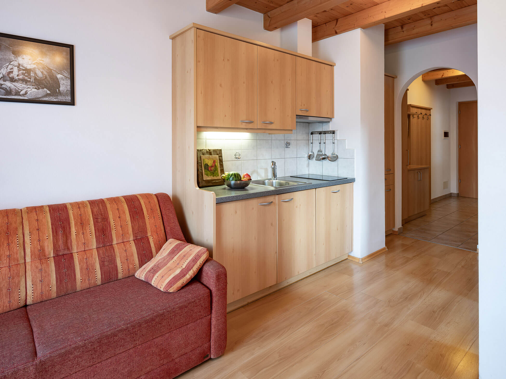 Rotes Sofa und daneben eine kleine Kochnische im Apartment Dreifinger und Piz da Peres - Branterhof