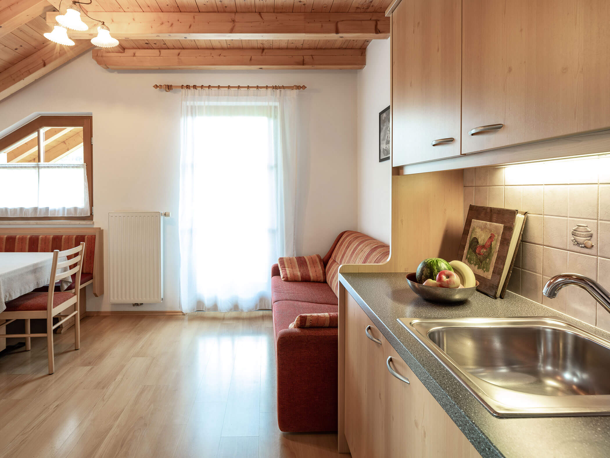 Wohn-Esszimmer mit rotem Sofa, Küche und Esstisch im Apartment Dreifinger und Piz da Pere - Branterhof