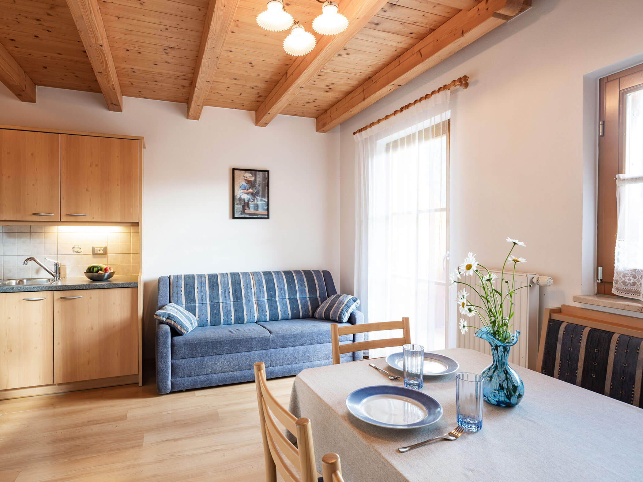 Wohn-Esszimmer mit blauem Sofa, gedeckten Esstisch und Küche im Apartment Dreifinger und Piz da Peres - Branterhof