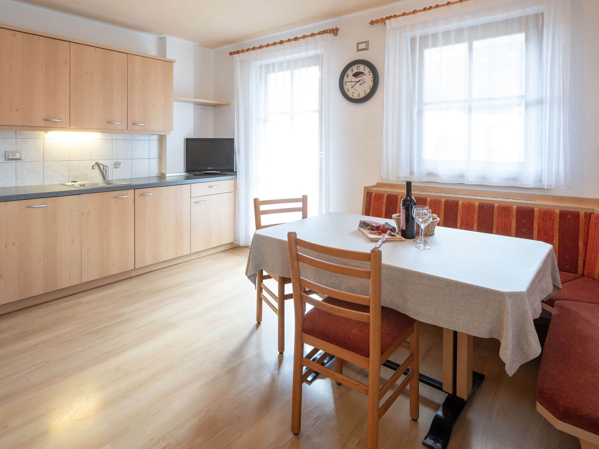 Esstisch mit zwei Weingläsern, eine Flasche Wein und Speck, daneben befindet sich die Küche im Apartment Hochnall - Branterhof