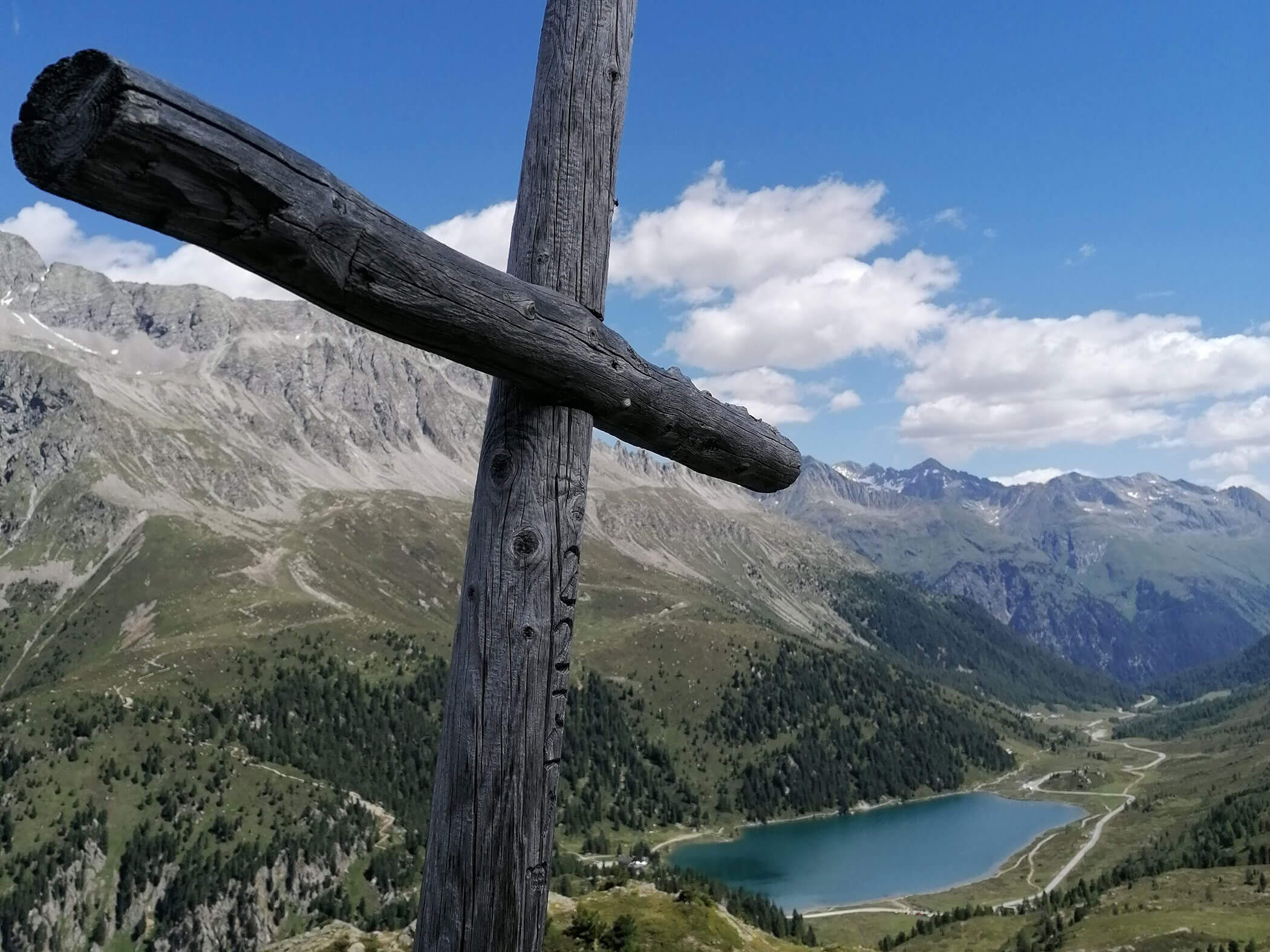 Gipfelkreuz mit Blick auf einen See und die Bergwelt von Südtirol - Branterhof