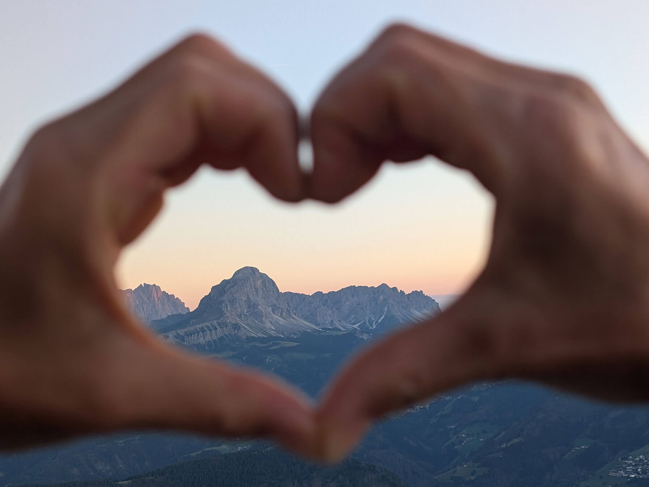 Herzförmige Hand und darin die Südtiroler Berge in der Abendsonne - Branterhof